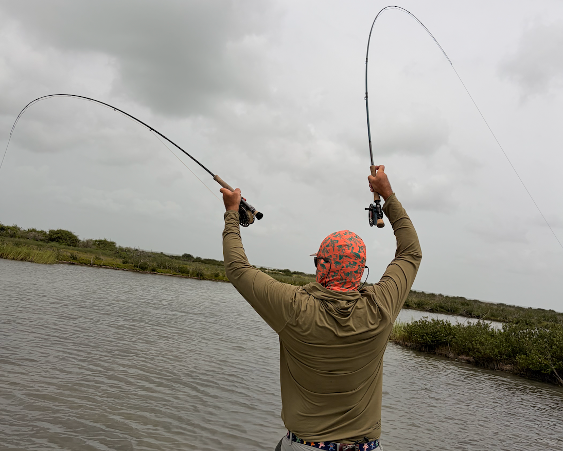 A man on a boat fishing in the water, holding up a bent fishing rod with both hands under a cloudy sky.